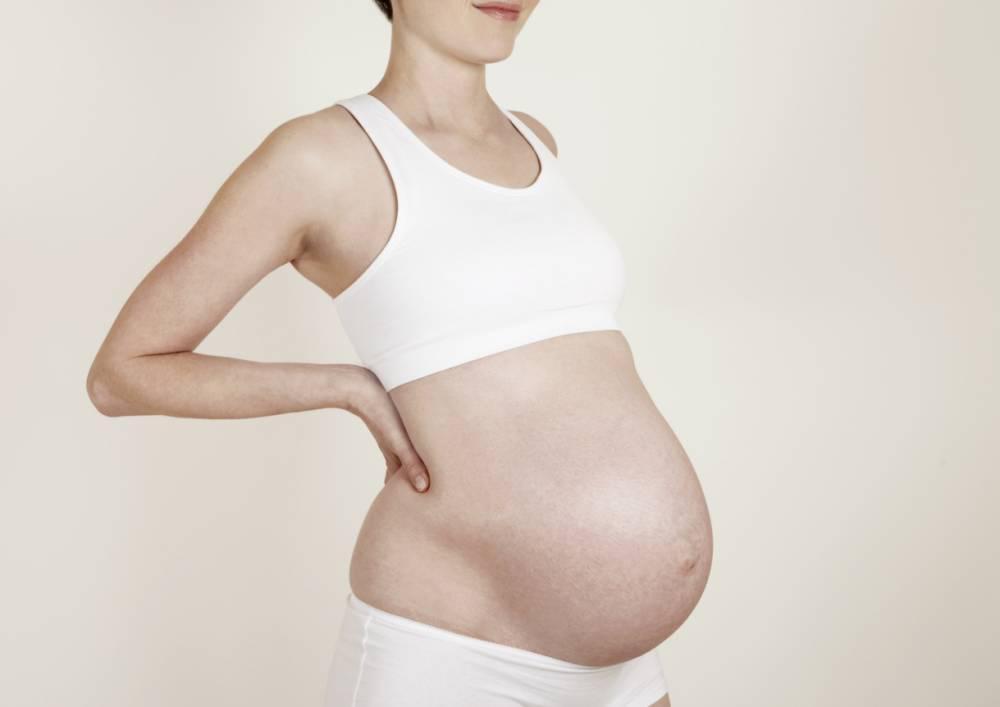 Pregnant woman in white underwear holding back