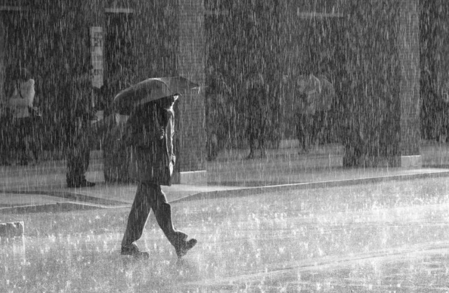 άνδρας με ομπρέλα περπατά στον δρόμο εν μέσω καταιγίδας