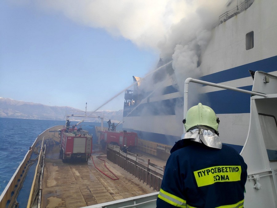 Πυροσβέστης σε πλοίο που μεταφέρει πυροσβεστικό όχημα, δίπλα από το φλεγόμενο καράβι Euroferry Olympia
