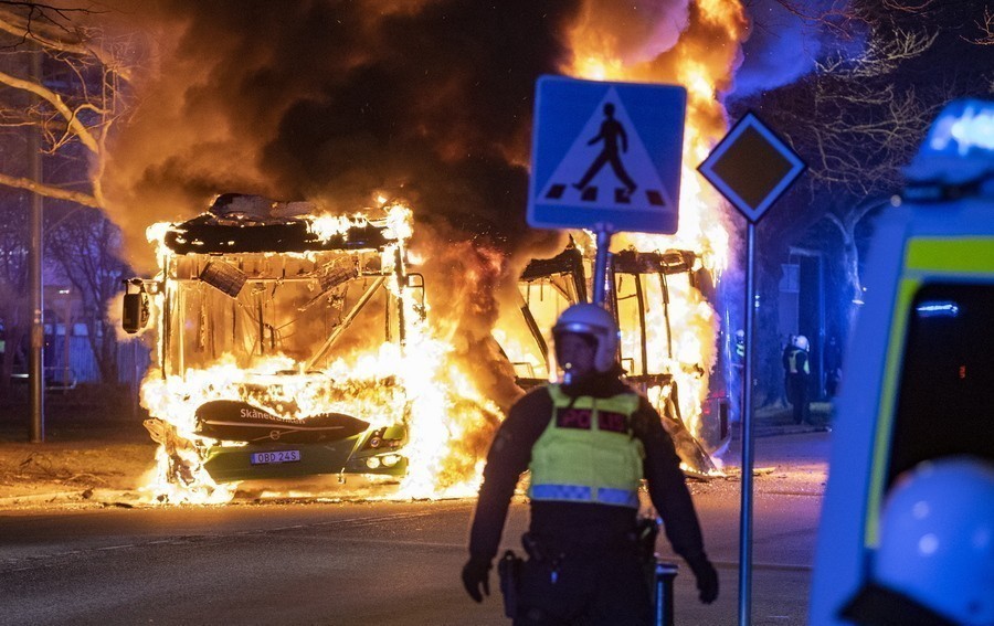 Αστυνομικός κοιτά ένα λεωφορείο στις φλόγες στην πόλη Rosengard στη Σουηδία