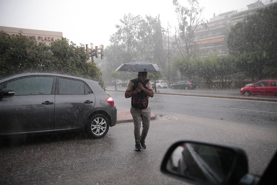 Άντρας με ομπρέλα περπατάει κατά τη διάρκεια έντονης βροχόπτωσης στην Αθήνα.