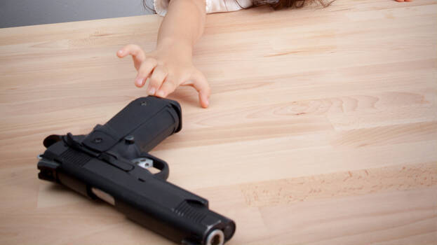 Ένα παιδί επιχειρεί να πιάσει ένα πιστόλι που βρίσκεται πάνω σε τραπέζι