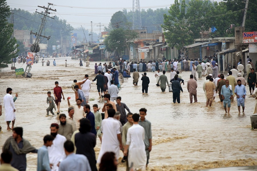 People wade through a flooded area following heavy rains in Charsadda District, Khyber Pakhtunkhwa province, Pakistan, 27 August 2022.