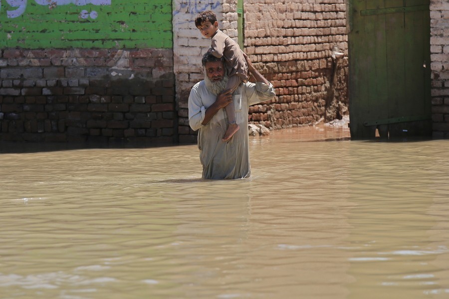 άνδρας κρατά στους ώμους του ένα παιδί και διασχίζει πλημμυρισμένο δρόμο στο Πακιστάν