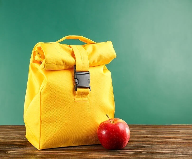 Μία κίτρινη σχολική τσάντα και ένα μήλο για τη σωστή διατροφή των παιδιών στο σχολείο