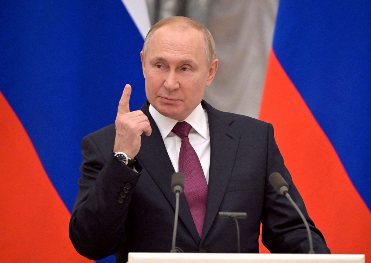 Βλαντιμίρ Πούτιν μπροστά από ρωσικές σημαίες με σηκωμένο το δάχτυλο του δεξιού χεριού του