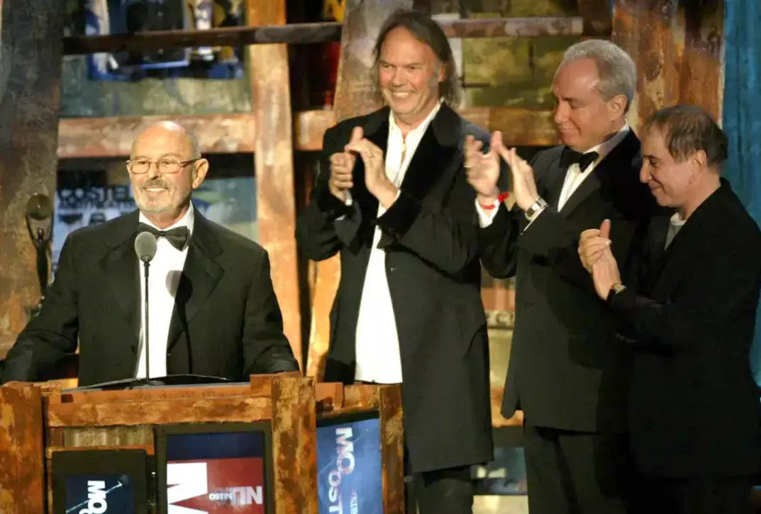 Ο Μο Όστιν (αριστερά) ενώ χειροκροτείται από τον Νιλ Γιανγκ, τον κινηματογραφικό –τηλεοπτικό παραγωγό Λορν Μάικλς και τον Πολ Σάιμον (2003)