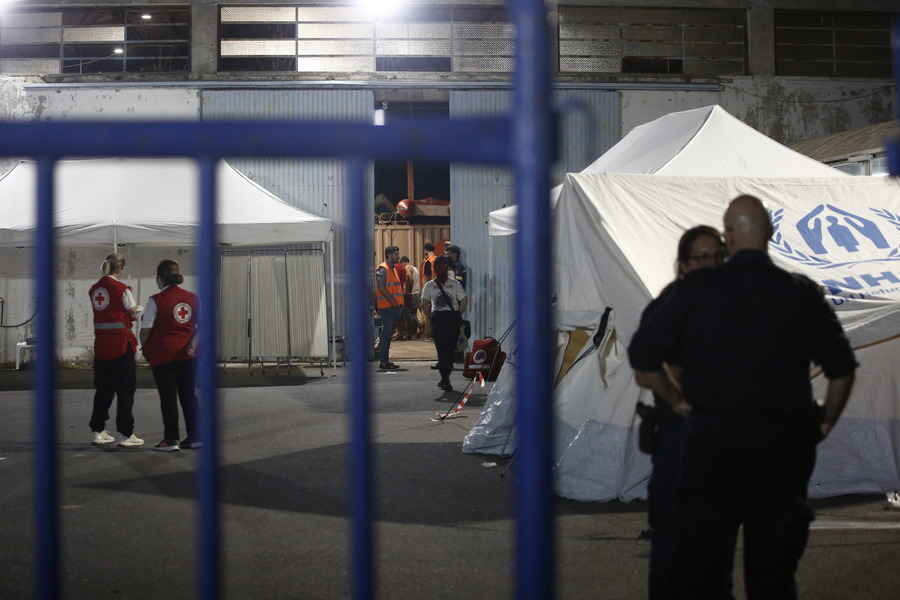 Διασώστες και εθελοντές στέκονται έξω από αποθήκη όπου διαμένουν προσωρινά διασωθέντες πρόσφυγες και μετανάστες μετά το πολύνεκρο ναυάγιο που έγινε ανοικτά της Πύλου, στο λιμάνι της Καλαμάτας