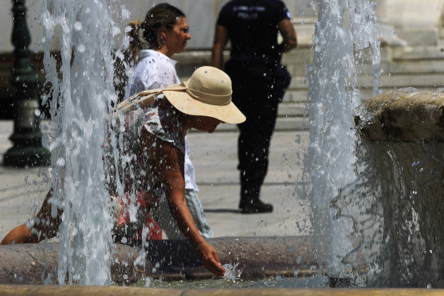 Γυναίκα δροσίζεται με το νερό από to συντριβάνι στην πλατεία Συντάγματος, κατά τη διάρκεια του καύσωνα