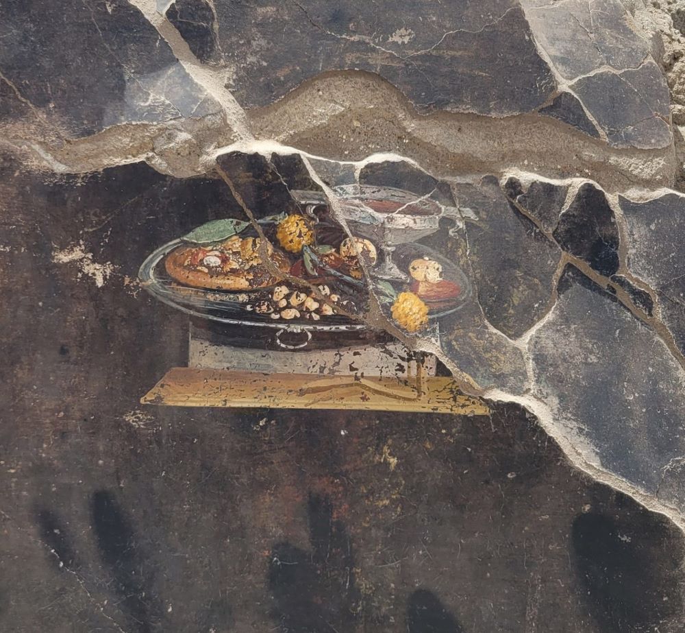 Τοιχογραφία με παράσταση πίτας ψωμιού που παραπέμπει σε πρόδρομο της πίτσας. Στο Αρχαιολογικό Πάρκο Πομπηίας