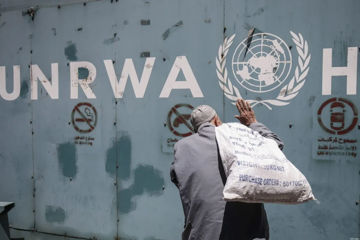 Παλαιστήνιος μεταφέρει σάκο με βοήθεια από την UNRWA, μπροστά από κτήριο με το σήμα της υπηρεσίας του ΟΗΕ