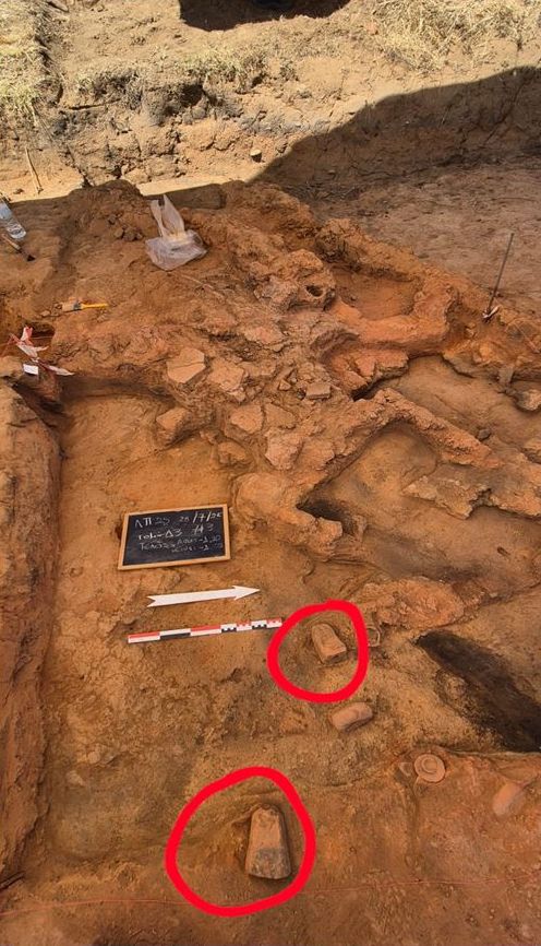 Το εσωτερικό του σπιτιού όπου διακρίνονται εστία και καμένες σανίδες στο δάπεδο. Κοντά στην εστία δύο πήλινοι κρατευτές.